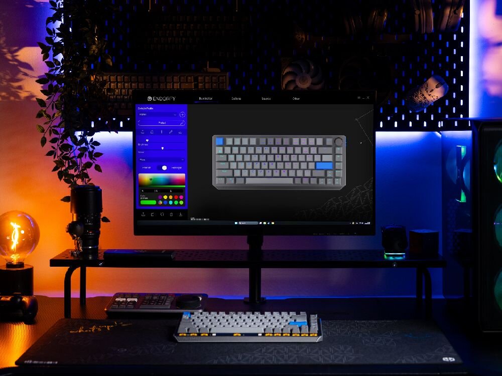 Na biurku znajduje się klawiatura mechaniczna z podświetleniem RGB, a na monitorze wyświetlony jest interfejs oprogramowania do jej konfiguracji. W tle widoczne są elementy dekoracyjne i komputer stacjonarny z podświetleniem LED.