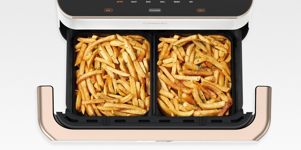 Obraz przedstawia frytkownicę beztłuszczową z dwoma koszami wypełnionymi frytkami. Na panelu widoczne są przyciski z napisami: \'AIR FRY\', \'ROAST\', \'BAKE\', \'GRILL\', \'HEAT\', \'DRY\'.