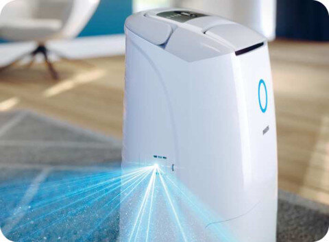 Na obrazie widoczny jest biały osuszacz powietrza z niebieskim podświetleniem i logo PHILIPS. Urządzenie stoi na dywanie, a z jego boku emitowane są niebieskie promienie świetlne.