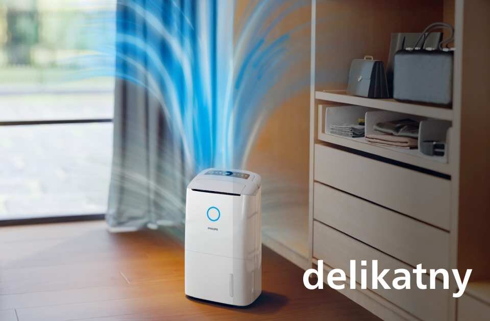 Na obrazie znajduje się biały osuszacz powietrza marki PHILIPS z niebieskim podświetleniem, z którego wydobywają się niebieskie strumienie powietrza. W prawym dolnym rogu widoczny jest napis \'delikatny\'.