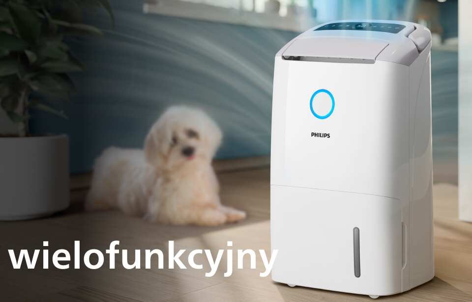 Na podłodze stoi biały osuszacz powietrza z logo PHILIPS, obok którego leży pies. Na obrazie widoczny jest napis \'wielofunkcyjny\'.