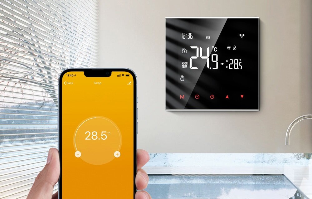 Na obrazie widoczny jest nowoczesny termostat z wyświetlaczem pokazującym temperaturę 24,9°C oraz smartfon z aplikacją ustawioną na 28,5°C. W tle znajduje się okno z żaluzjami.