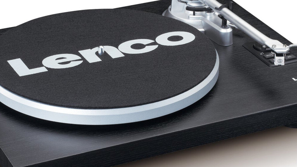 Na zdjęciu widoczny jest czarny gramofon z napisem \'Lenco\' na talerzu. Gramofon ma srebrne ramię i jest wykonany z ciemnego materiału.
