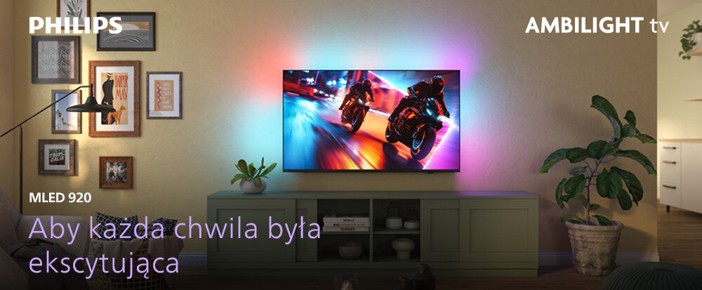 Na ścianie wisi telewizor wyświetlający dynamiczną scenę z motocyklami, otoczony kolorowym światłem Ambilight. Na obrazie widoczne są napisy: \'PHILIPS\', \'AMBILIGHT tv\', \'MLED 920\', \'Aby każda chwila była ekscytująca\'.