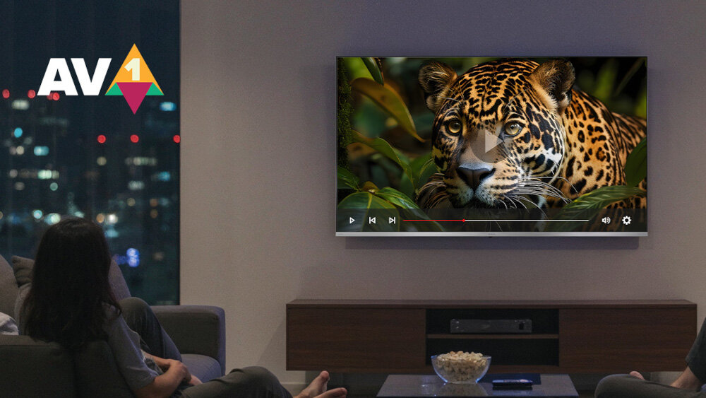 Na ścianie wisi telewizor wyświetlający obraz jaguara w dżungli. W rogu ekranu widoczne jest logo \'AV1\'.