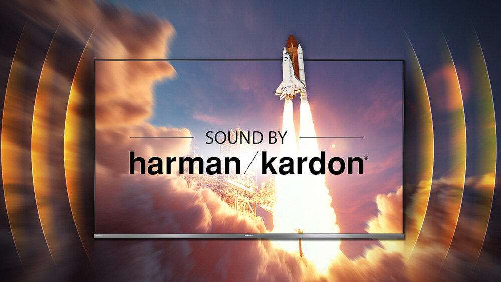 Obraz przedstawia startujący prom kosmiczny na tle nieba z chmurami, widoczny na ekranie telewizora. Na ekranie znajduje się tekst: \'SOUND BY harman/kardon\'.