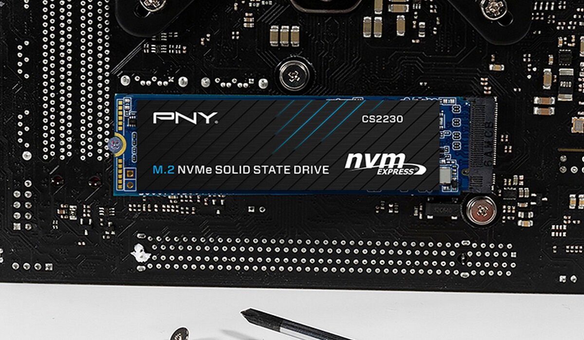 Na obrazie widoczny jest dysk SSD z napisem \'PNY M.2 NVMe SOLID STATE DRIVE nvm express\' zamontowany na płycie głównej. Obok leży mały śrubokręt.