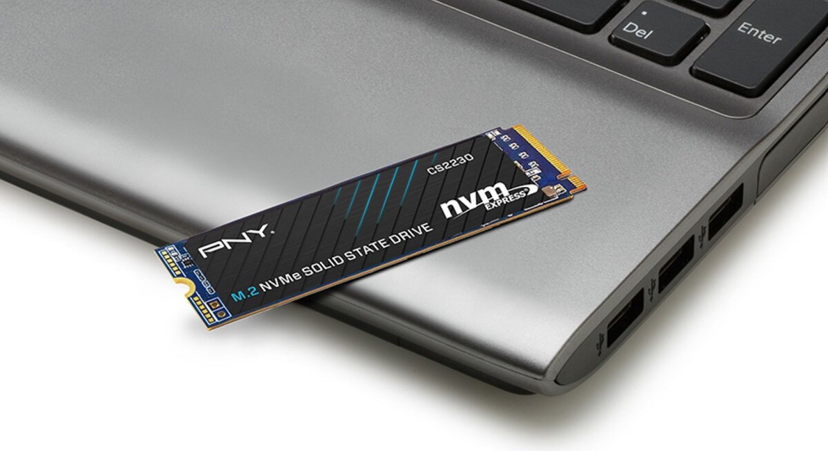 Na obrazie widoczny jest dysk SSD z napisem \'PNY M.2 NVMe SOLID STATE DRIVE\' umieszczony na laptopie. Obok znajduje się klawiatura z widocznymi klawiszami \'Del\' i \'Enter\'.