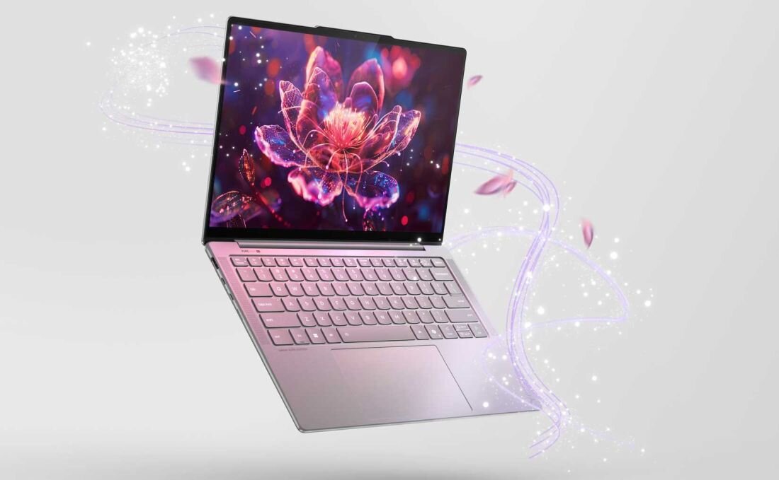 Laptop z otwartym ekranem, na którym wyświetlany jest obraz kwiatu z efektami świetlnymi. Klawiatura jest widoczna, a wokół laptopa unoszą się świetliste efekty i płatki.