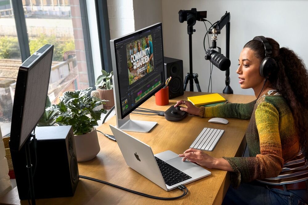 APPLE MacBook Pro 2026 14 Retina M5 Max 1TB SSD macOS sprzętu i systemu macOS Secure Enclave dane biometryczne klucze szyfrowania Touch ID FileVault Znajdź - Kobieta w słuchawkach pracująca przy stanowisku z mikrofonem, dodatkowym monitorem i otwartym urządzeniem