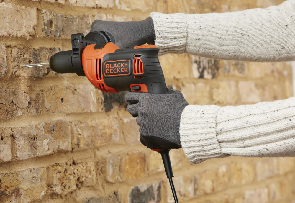 Wiertarka udarowa BLACK&DECKER BEH710-QS ceglana ściana osoba trzyma wiertarkę w dłoni wierci otwór w ścianie ergonomiczna konstrukcja niska waga (1,96 kg) wygodna w obsłudze długość przewodu zasilającego około 2,5 m niewielkie wymiary dobrze leży w dłoni