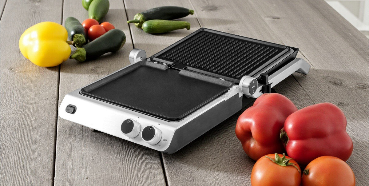 Grill elektryczny GASTROBACK 42537, open-grill, płyta, ryflowana, gładka, grill z otwartymi płytami stoi na drewnianym blacie w tle warzywa