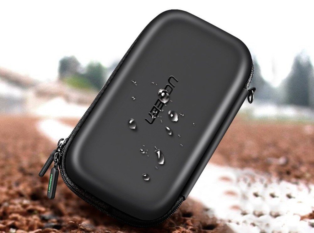 Etui na dysk UGREEN 50274 LP128 Zamknięte czarne etui leżące pod skosem na brązowym podłożu, z widocznymi kroplami wody na powierzchni obudowy oraz napisem 'UGREEN'