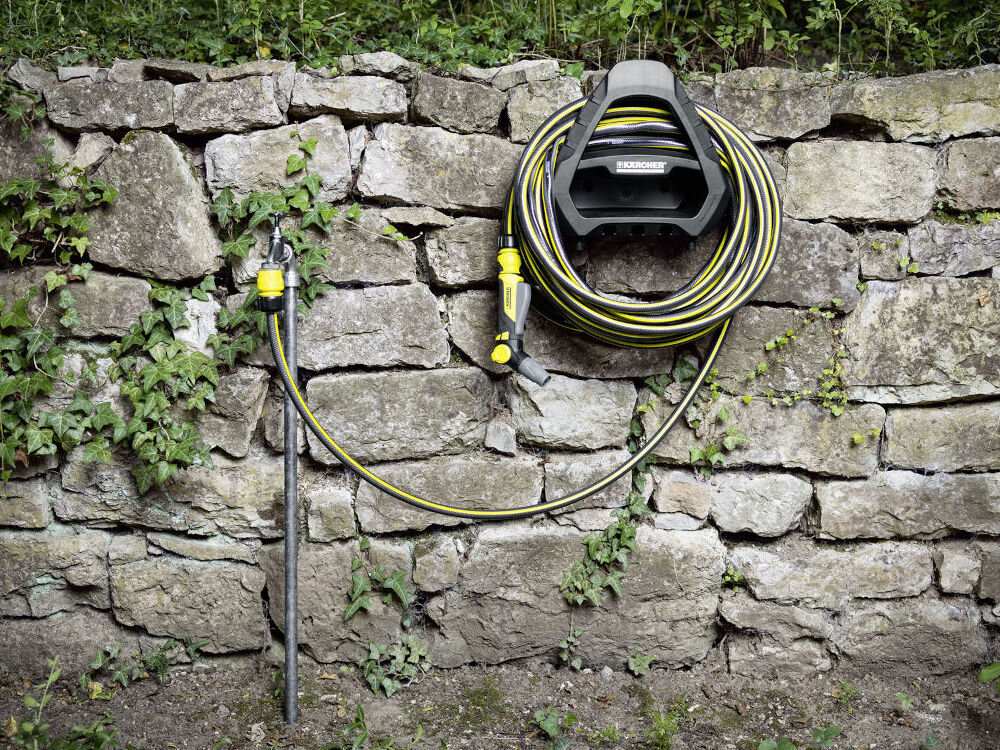 Wąż ogrodowy KARCHER PrimoFlex Plus 3/4 25 m 2.645-323.0, woda, podlewanie, ogród, rośliny, w tle mur kamienny, na nim zawinięty na haku wąż wraz z myjką