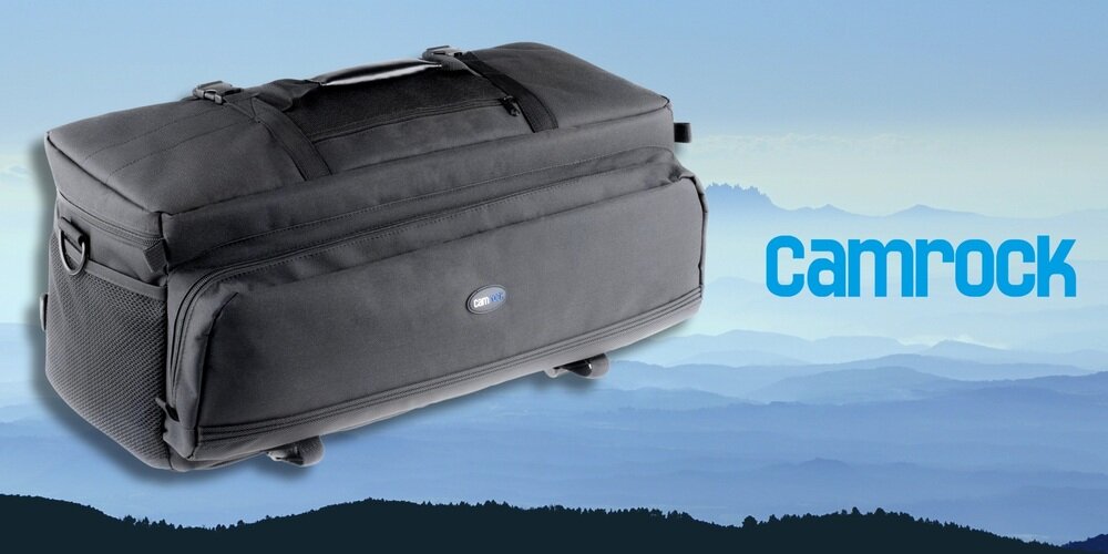 Czarna torba fotograficzna Camrock Tank X65 ustawiona pod kątem na tle gór i logo Camrock, widoczne kieszenie boczne.