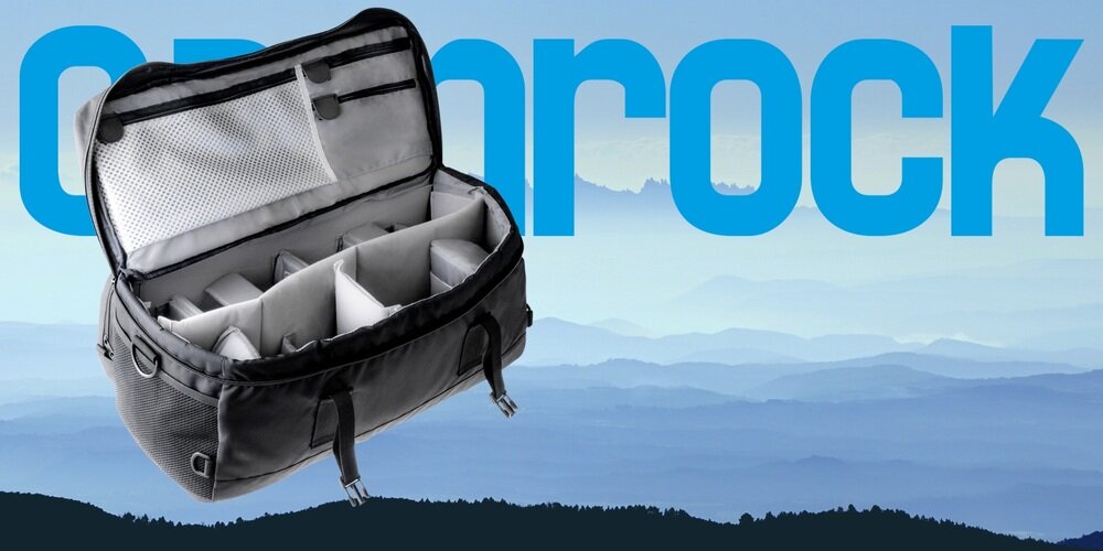 Torba Camrock Tank X65 otwarta, z widocznymi pustymi przegrodami i kieszeniami w klapie, na tle gór i dużego logo Camrock.