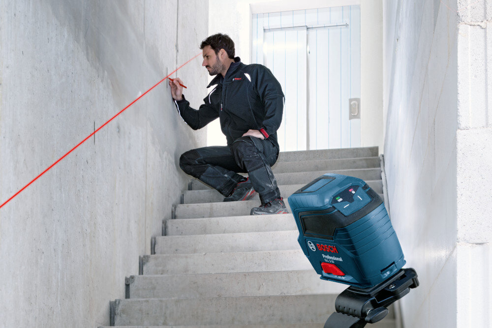Laser liniowy BOSCH Professional GLL 2-10 0601063L00 pomieszczenie plac budowy schody betonowa ściana osoba wyznacza linie na ścianie laser ustawiony na uchwycie dokładność na poziomie ±0,3 mm/m zasięg do 10 metrów w trybie skrzyżowanych linii równa linia montażu bez ryzyka odchyleń