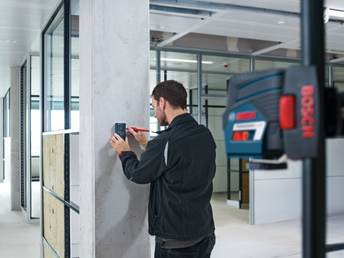 Odbiornik laserowy BOSCH Professional LR 6 (0601069H00), laser, odbiornik, pomiar, wiązka, odbiornik trzymany przy ścianie przez mężczyznę na placu budowy