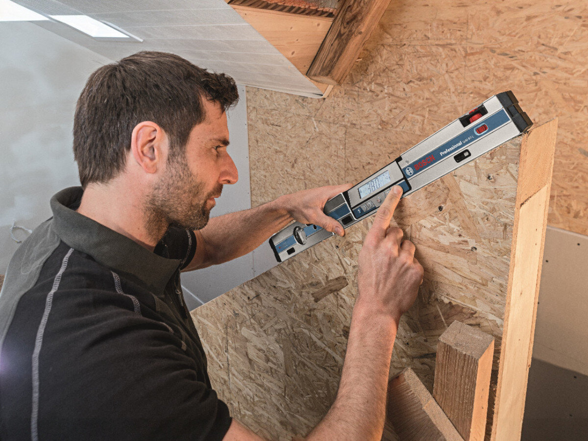 Osoba używa poziomnicy laserowej BOSCH GIM 60 L Professional na drewnianej konstrukcji. Na poziomnicy widoczne jest logo BOSCH i napis \'Professional\'.