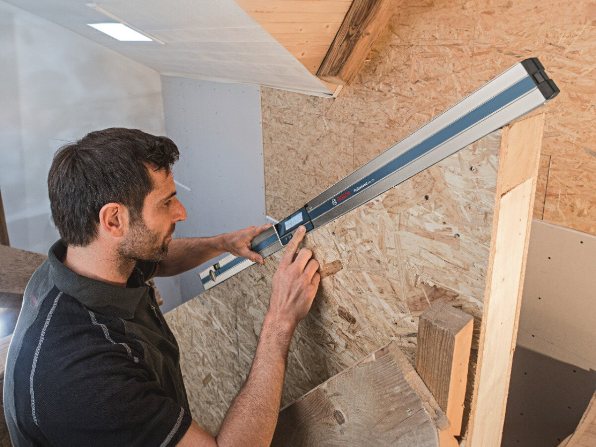 Osoba używa elektronicznej poziomnicy BOSCH GIM 120 Professional do pomiaru na drewnianej konstrukcji. Na poziomnicy widoczne jest logo BOSCH oraz wyświetlacz elektroniczny.