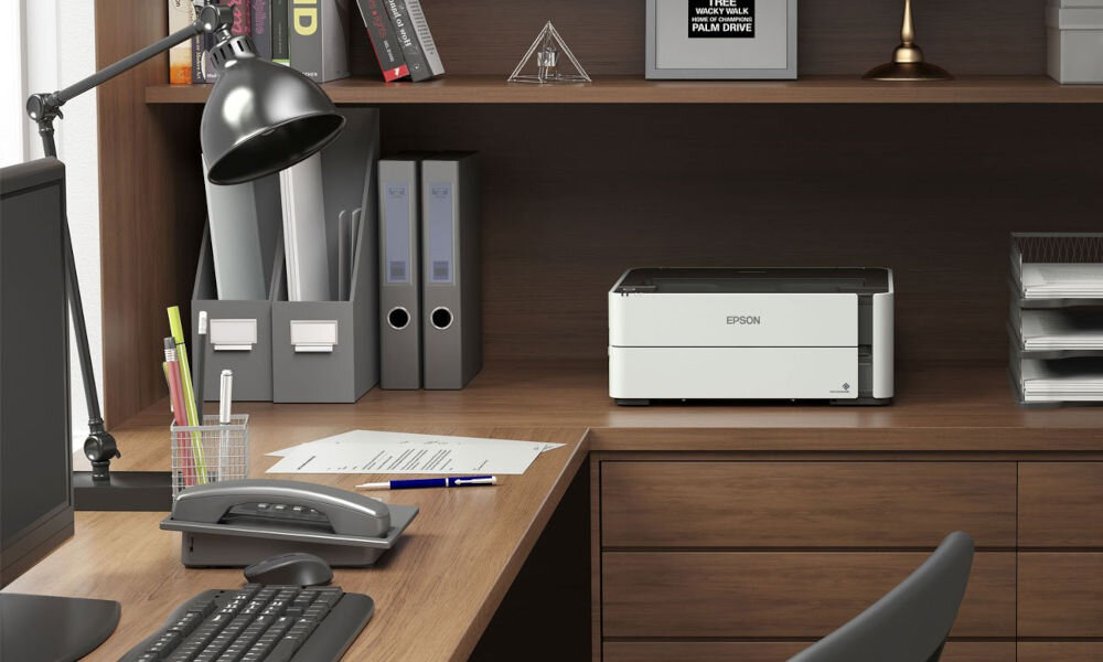Drukarka EPSON EcoTank M1170 Automatyczny druk dwustronny, Wi-Fi prezentacja drukarki w pokoju biurowym na biurku monitor klawiatura dokumenty telefon lampka - drukarka do biura z Wi-Fi i dwustronnym drukiem