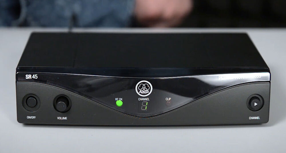 Zestaw bezprzewodowy AKG WMS45 Sport Set Band A prezentacja odbiornika na blacie w tle osoba bezprzewodowa transmisja zasięg swobodne poruszanie się po sali