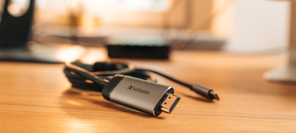 Na drewnianym blacie leży kabel z końcówką HDMI, na której widnieje logo \'Verbatim\'.