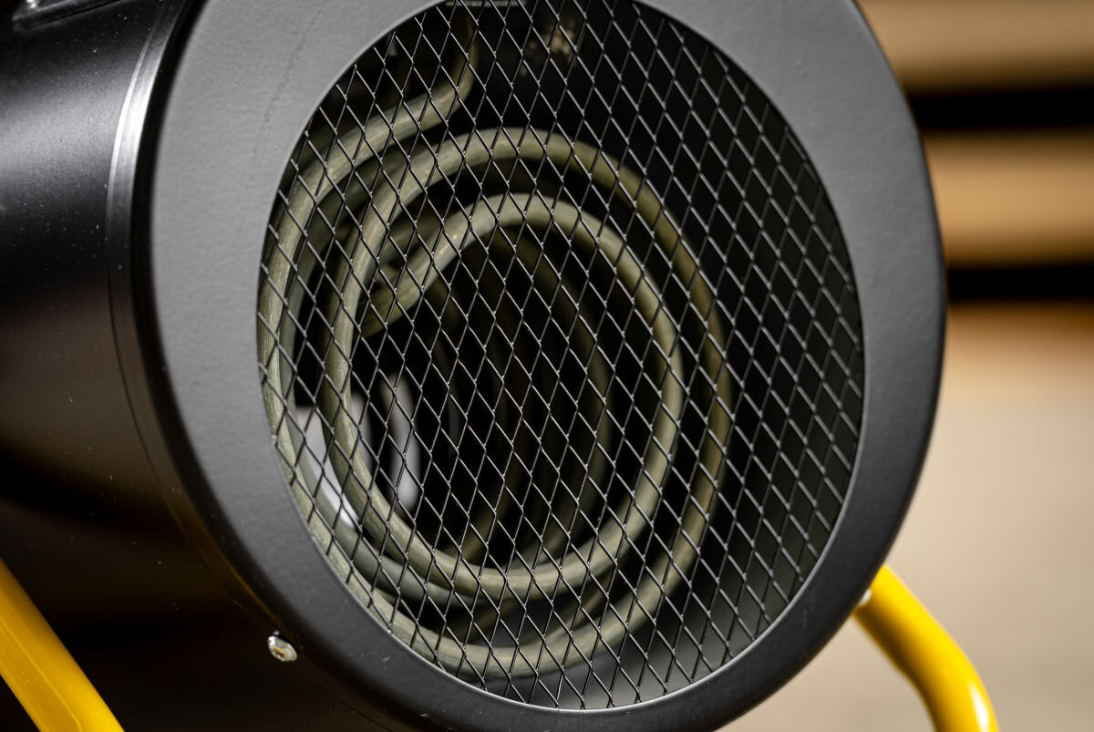 Nagrzewnica elektryczna DEDRA DED9932B, wentylator, cyrkulacja, grzałka, równomierność, Zbliżenie na spiralną grzałkę nagrzewnicy DEDRA DED9932B za siatką ochronną, żółty uchwyt.