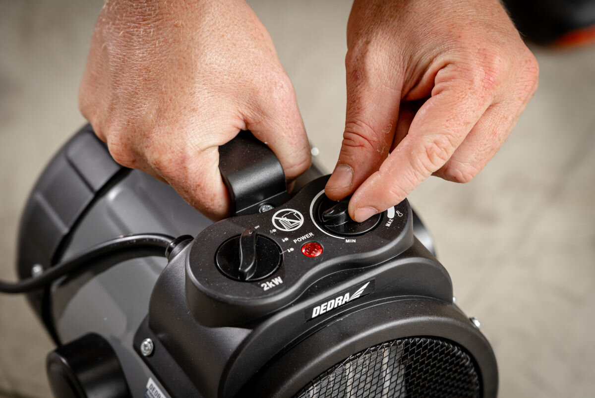 Nagrzewnica elektryczna DEDRA DED9930C2, termostat, moc, oszczędność, automatyka, Ręce obracają pokrętło regulacji temperatury na panelu nagrzewnicy Dedra DED9930C2.