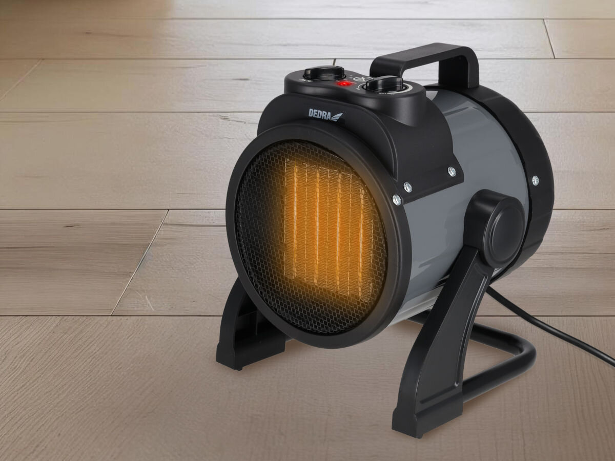 Nagrzewnica elektryczna DEDRA DED9930C2, zabezpieczenie, metal, stabilność, IP20, Dedra DED9930C2 ogrzewa jasną podłogę deskową, widoczna grillowana osłona i żółty stojak.