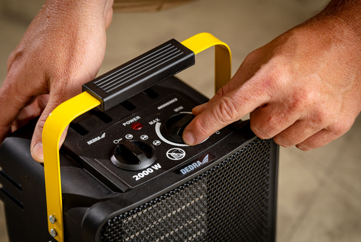 Nagrzewnica elektryczna DEDRA DED9930C3, termostat, pokrętła, oszczędność, automatyka, Ręka reguluje temperaturę na panelu nagrzewnicy Dedra DED9930C3, widoczny czarny panel.