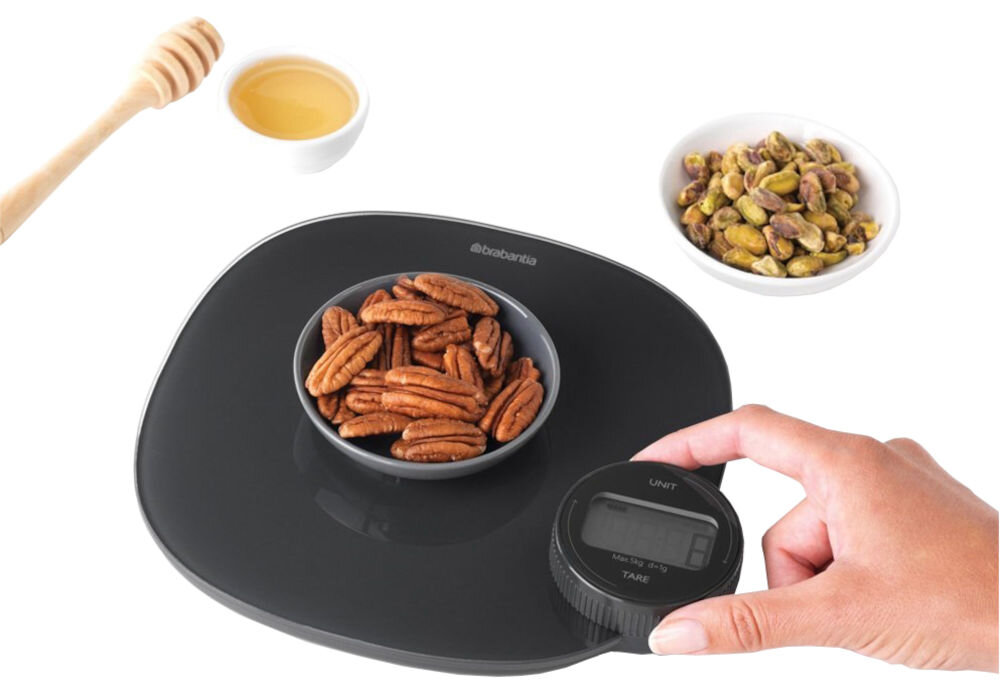 Waga kuchenna BRABANTIA Tasty+ 122880 Ciemnoszary precyzyjne ważenie białe tło ciemna waga osoba kręci za pokrętło miseczka ze składnikami na wadze 