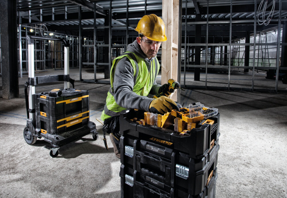Organizer DEWALT DT70716 TSTAK pomieszczenie hala metalowe konstrukcje osoba stoi przy wózku narzędziowym na wózku leży organizer w pełni kompatybilny z systemem TSTAK indywidualny system przechowywania modułowa konstrukcja