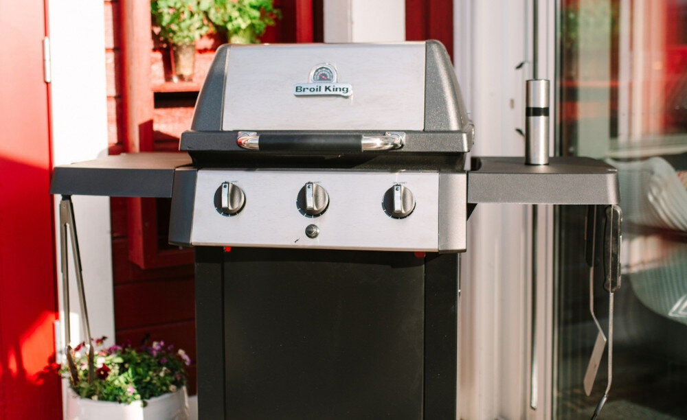 Grill gazowy BROIL KING GEM 310 6.9 kW 53 x 34 - 46.5 x 18.5 cm zbliżenie na górę grilla w tle dom rośliny wygoda wysoka jakość grillowania funkcjonalność solidne wykonanie wymiary 110 x 115 x 54 cm przemyślana konstrukcja praktyczne rozwiązania