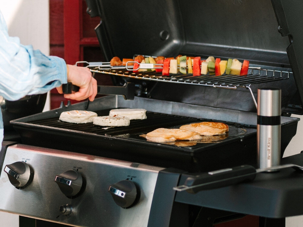 Grill gazowy BROIL KING GEM 310 6.9 kW 53 x 34 - 46.5 x 18.5 cm otwarta pokrywa grilla osoba grilluje potrawy łączna powierzchnia 2662,25 cm² dwa żeliwne ruszty górna półka do utrzymania ciepła grillowania pośredniego powolne dopiekanie potraw