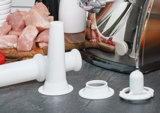 Zbliżenie na wymienne nasadki na blacie kuchennym. W tle deska z pokrojonym na kawałki mięsem.