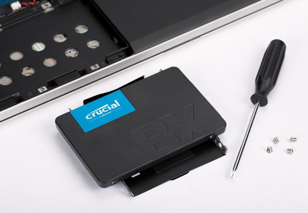 Dysk CRUCIAL BX500 Czarny dysk SSD i śrubokręt leżą na białej powierzchni obok rozkręconego laptopa i kilku małych śrubek, energooszczędność, pobór prądu