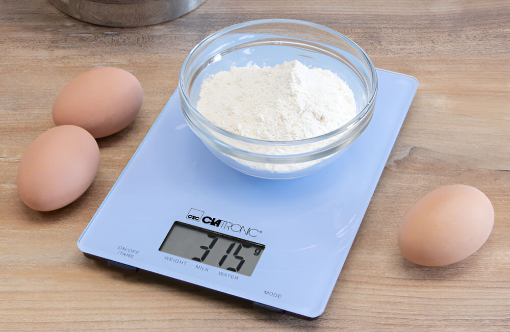 Waga kuchenna CLATRONIC KW 3626 Niebieski precyzyjne ważenie niebieska waga na blacie mąka w misce na wadze obok leżą jajka wyświetlacz