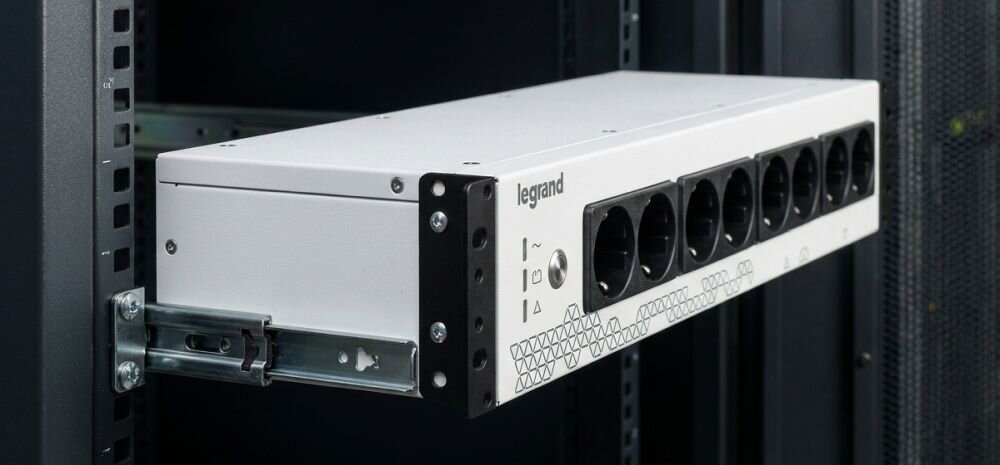 Na obrazie widoczny jest zasilacz UPS zamontowany w szafie serwerowej, z logo \'legrand\' na obudowie. Zasilacz posiada kilka gniazd elektrycznych na przednim panelu.