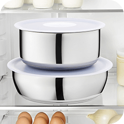 Dwa metalowe naczynia z białymi pokrywkami umieszczone w lodówce. W tle widoczne są jajka i inne produkty spożywcze.