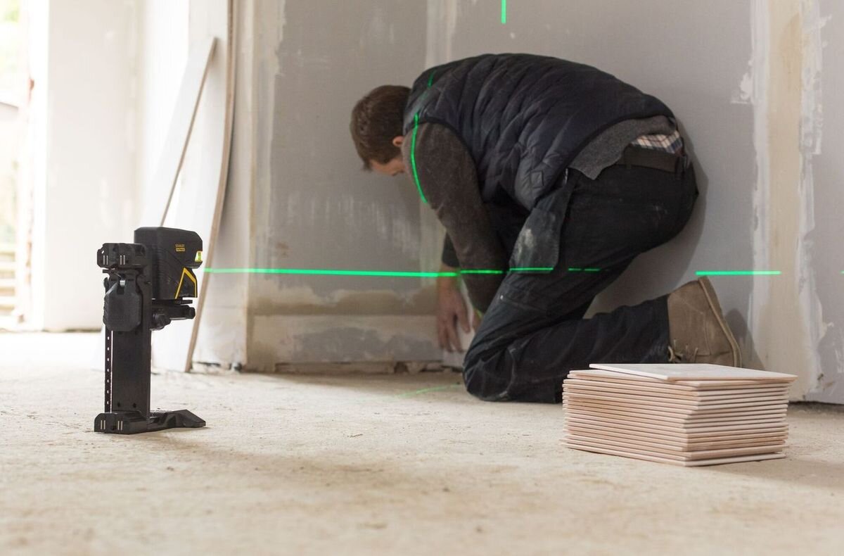 Laser punktowo-krzyżowy STANLEY FMHT77598-1, laser, budowa, pomiar, praca, Mężczyzna układa płytki przy pomocy lasera krzyżowego wyświetlającego zieloną linię.
