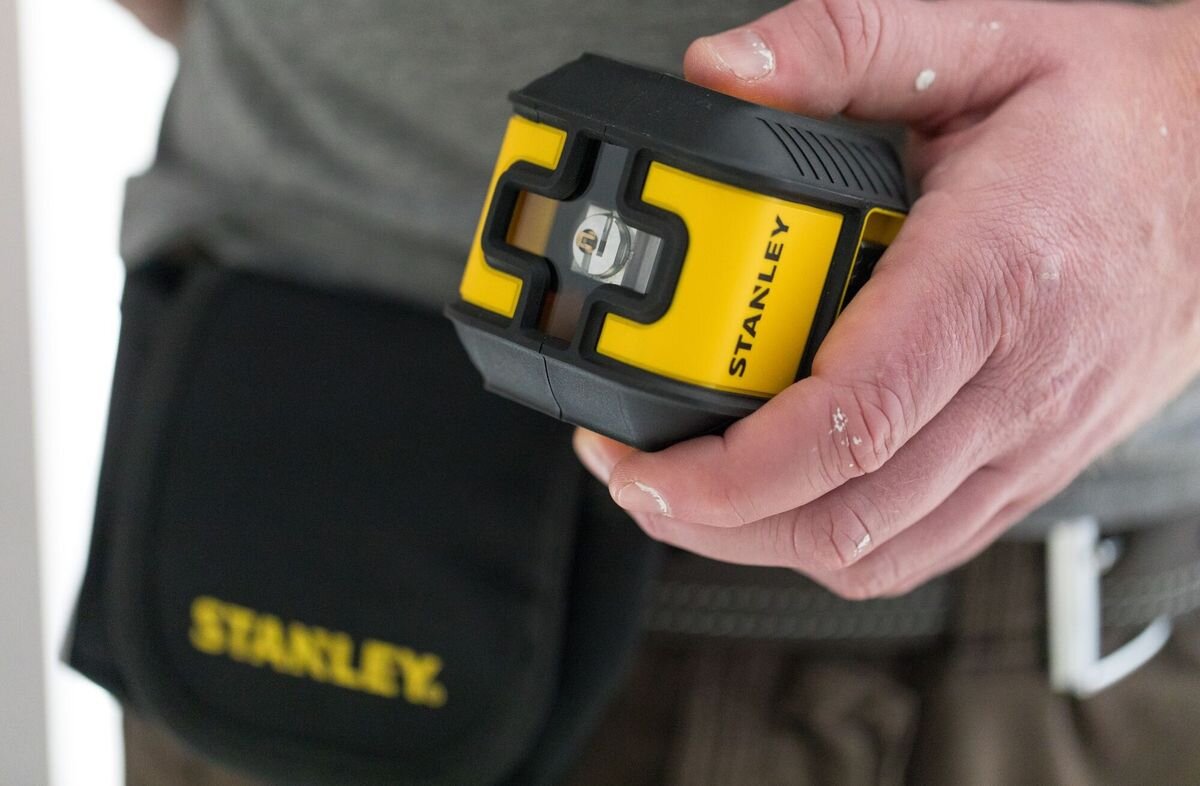 Laser krzyżowy STANLEY Cubix STHT77648-1, bateria, praca, czas, energia, Laser trzymany w dłoni w tle etui do schowania