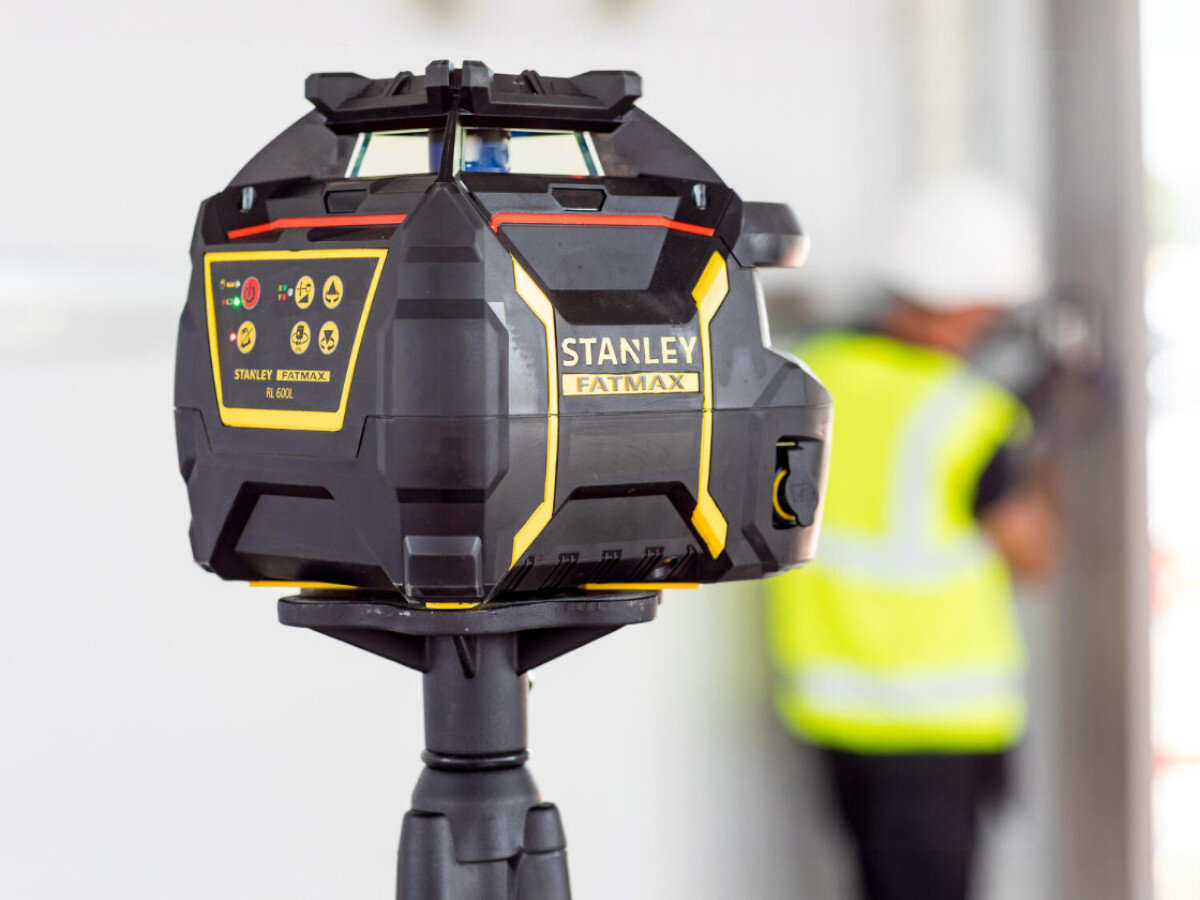 Niwelator laserowy STANLEY FMHT77449-1, zasięg, dokładność, pomiar, detektor, Laser rotacyjny Stanley zamontowany na statywie na tle rusztowań i pracownika z łatą.