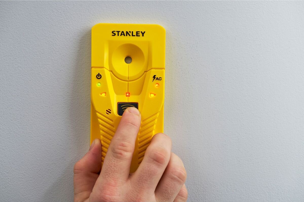 Wykrywacz profili STANLEY S110 STHT77587-0, kable, napięcie, bezpieczeństwo, prąd, dłoń trzyma wykrywacz profili do ściany