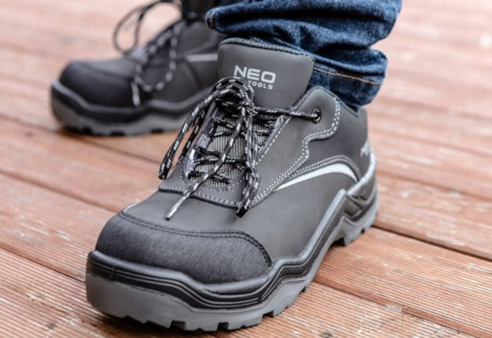 Półbuty robocze NEO 82-150-40 rozmiar 40 osoba stoi na drewianym podeście normy EN 20345 i EN ISO 20345:2022 wysoki standard ochrony certyfikat CE zgodność z rygorystycznymi europejskimi przepisami dla profesjonalistów i hobbystów