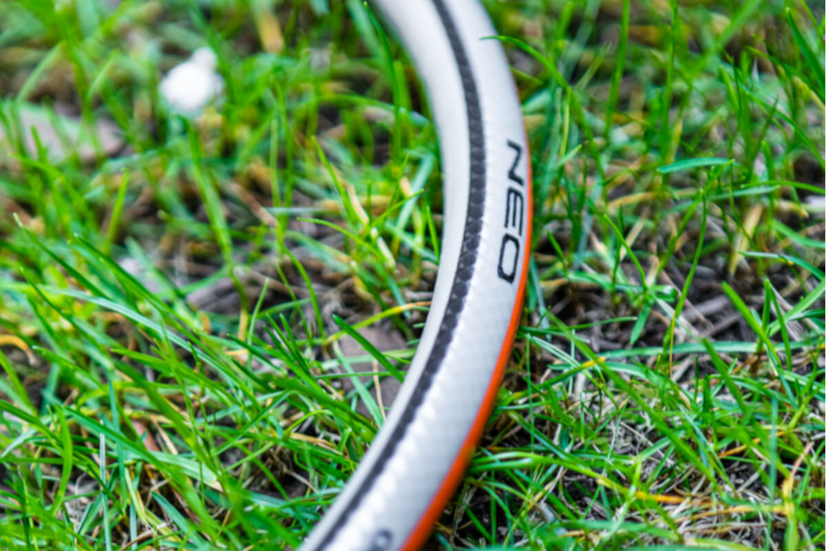 Wąż ogrodowy NEO Optima 3/4 50 m 15-825, zastosowanie, podlewanie, oda, pielęgnacja, na trawniku leży wąż z napisem NEO