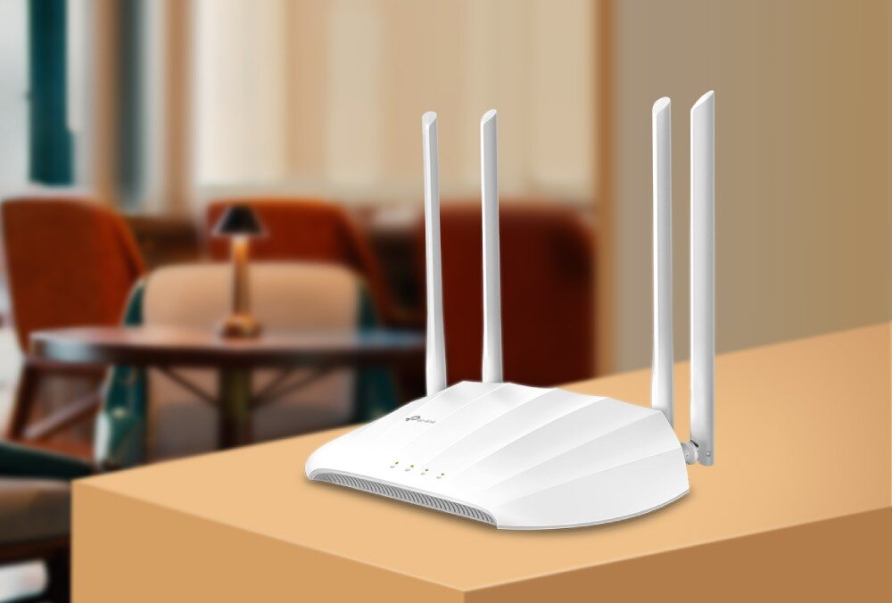 Punkt dostępu TP-LINK TL-WA1201 Urządzenie sieciowe z czterema antenami ustawione na blacie w tle wnętrza z fotelami i stolikiem, opis