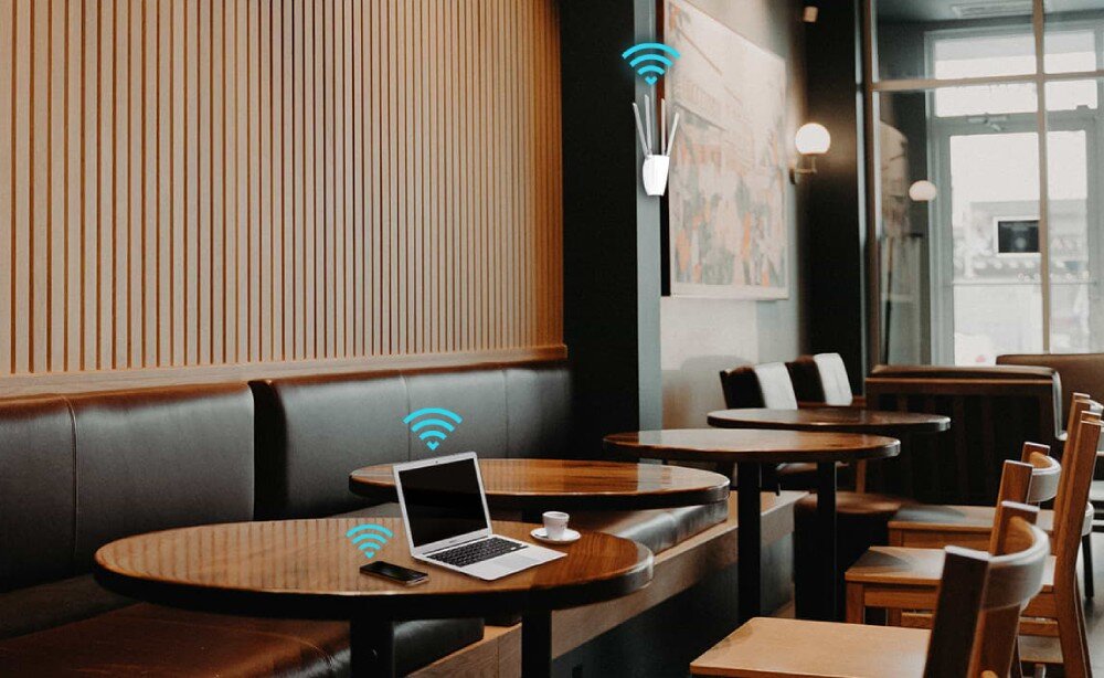Punkt dostępu TP-LINK TL-WA1201 Wnętrze kawiarni z urządzeniem sieciowym zamontowanym na ścianie i ikonami sygnału Wi-Fi przy stolikach z laptopem i telefonem, zasilanie PoE, montaż