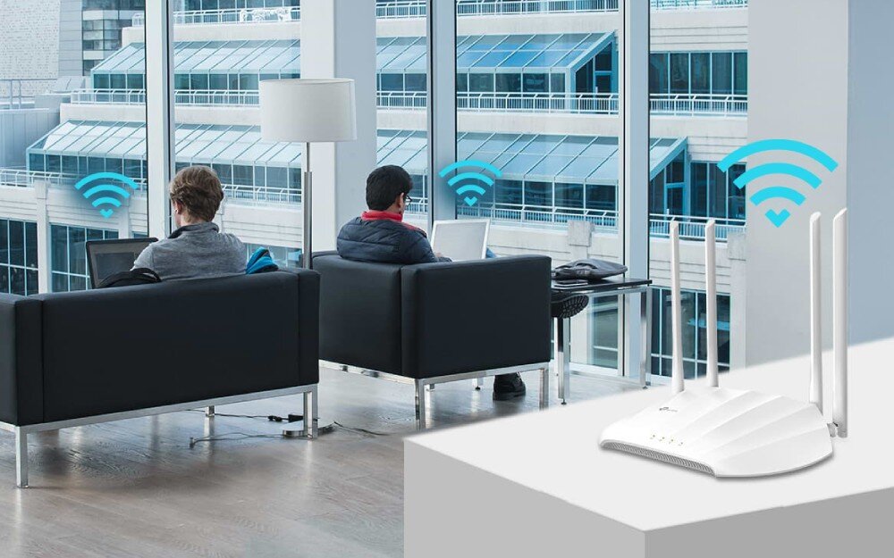 Punkt dostępu TP-LINK TL-WA1201 Dwie osoby korzystające z laptopów w przestrzeni biurowej, obok urządzenia sieciowego wysyłającego sygnał Wi-Fi, zabezpieczenia, firewall, szyfrowanie