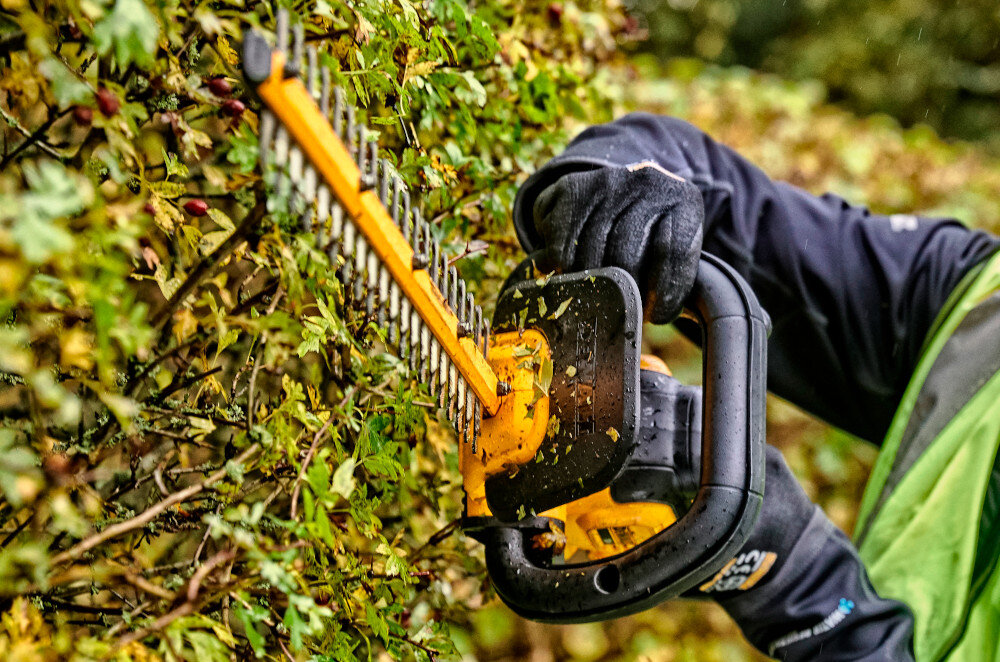Nożyce do żywopłotu DEWALT DCMHT563N-XJ 18V akumulatorowe ogród zbliżenie na uchwyt osoba trzyma nożyce w dłoniach uchwyt w kształcie litery D wygodna obsługa w różnych pozycjach dłoni precyzja pracy ogranicza ryzyko nierównego cięcia swoboda zmiany chwytu